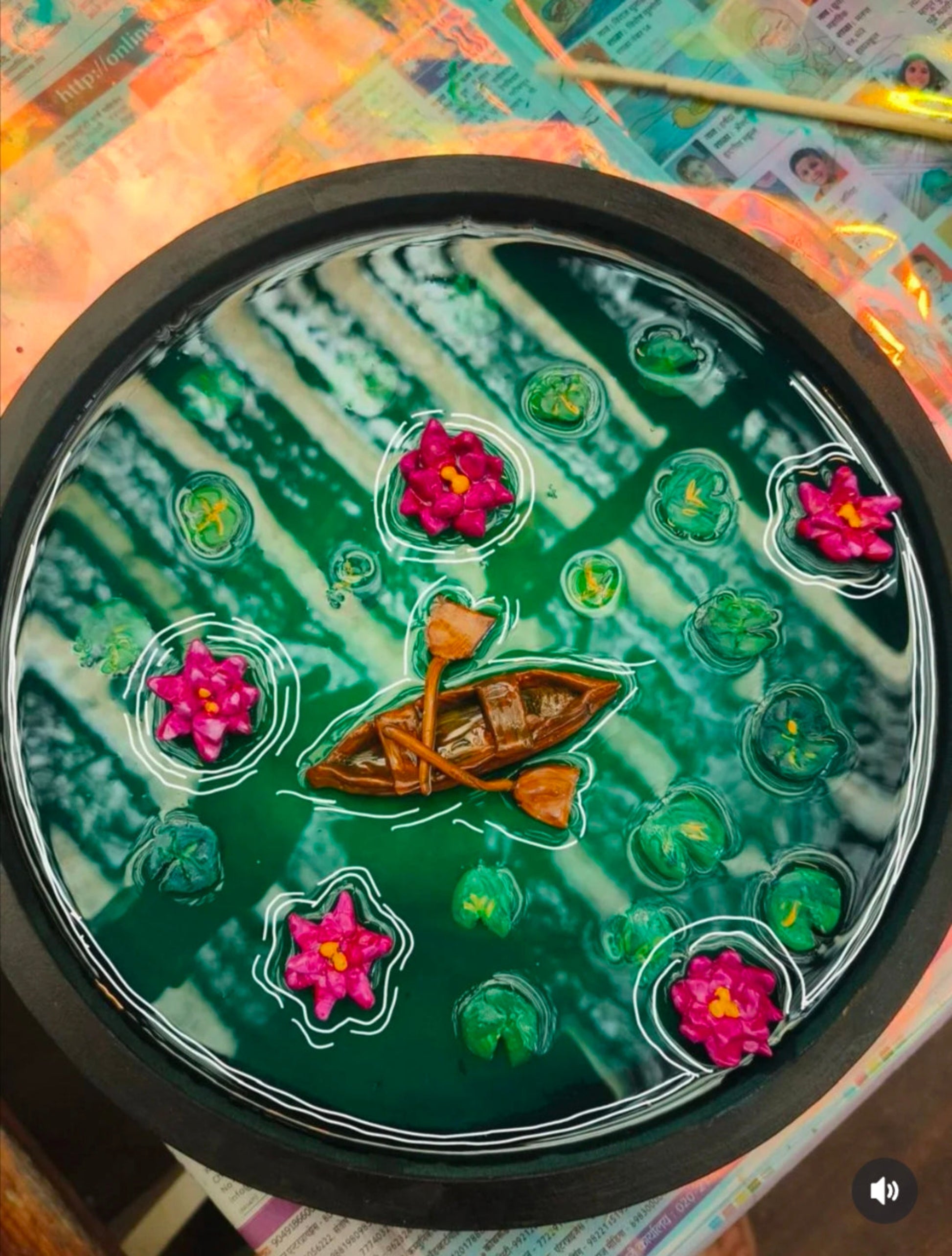 Artistic depiction of a boat on water with pink flowers and green lily pads in a circular frame.